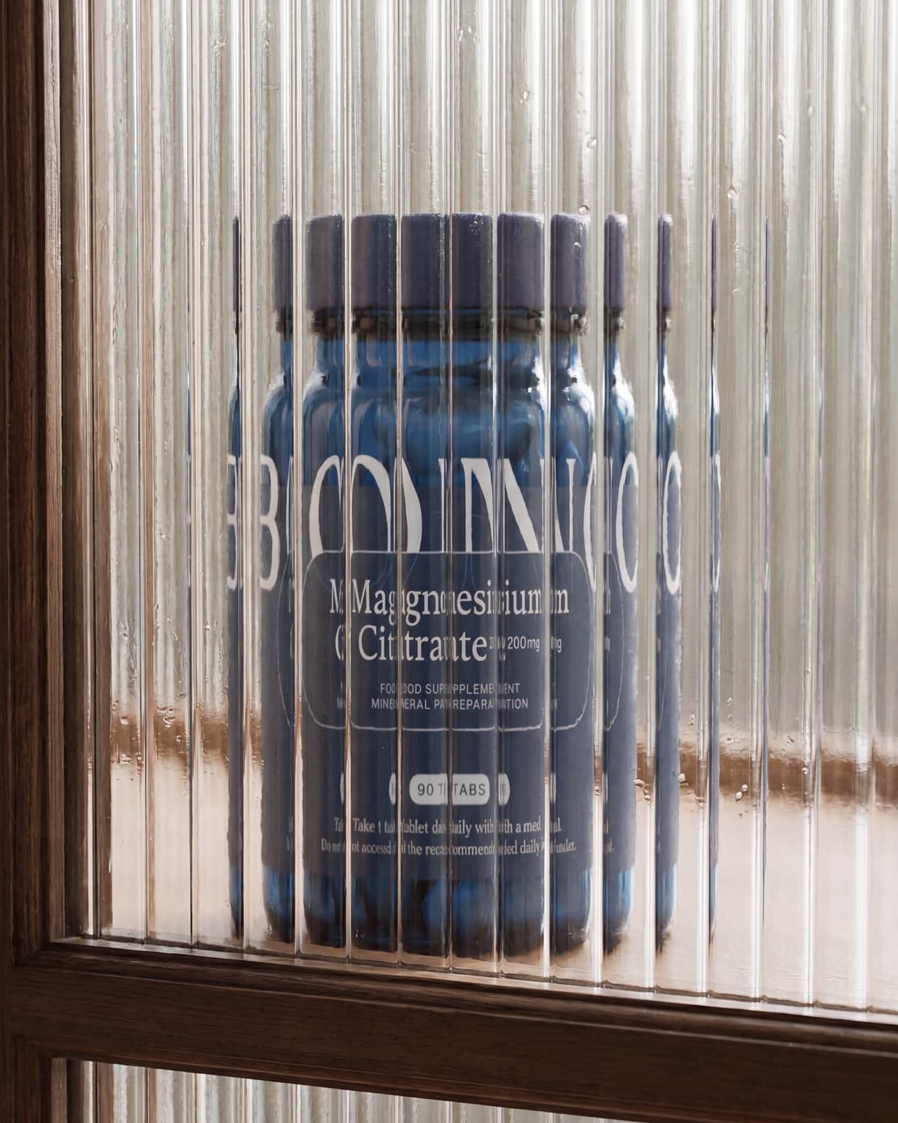 A jar of BONO Supplements Magnesium Citrate behind ribbed glass